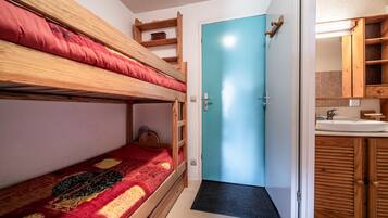 A bunk bed with a red blanket, a blue door, and a wooden cabinet with a mirror.