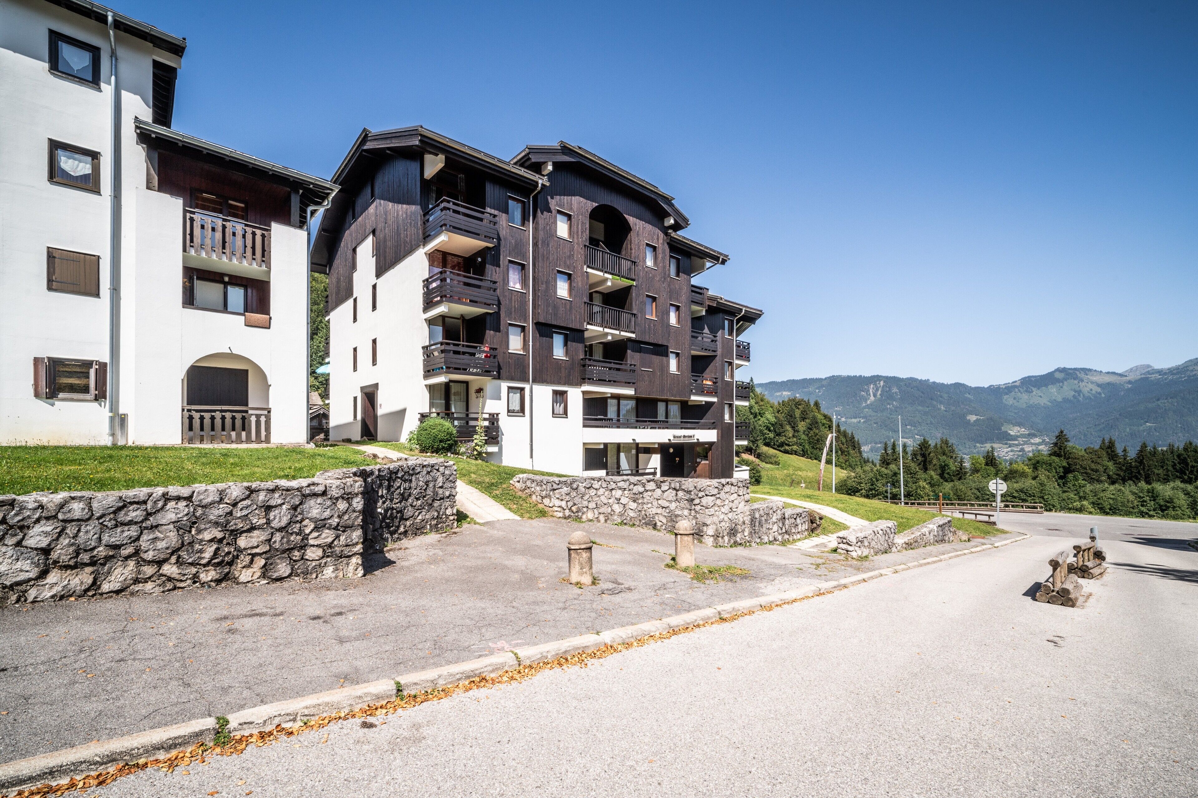 A multi-story hotel with balconies, stone walls, and a view of mountains.