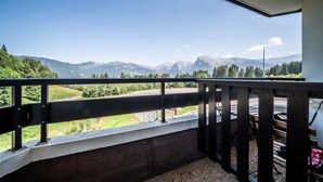 Un balcon donnant sur un paysage montagneux, une route et une voiture garée.