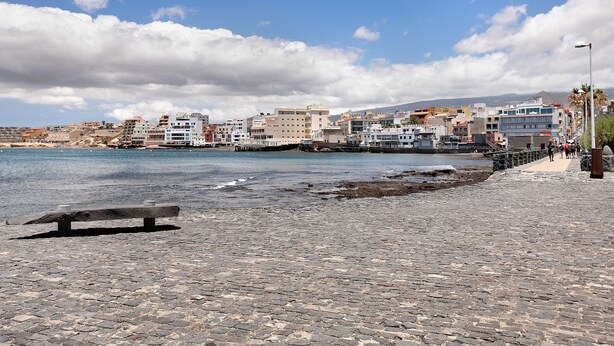 A cobblestone waterfront promenade with a bench, buildings in the background, and a clear sky. - Medano Beach Home Ocean View Apartment with Sea Views, Balcony and Wi-Fi (El Medano)