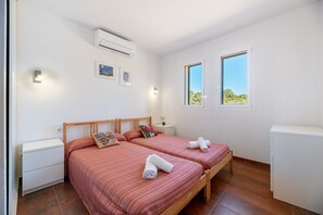 Ein Schlafzimmer mit zwei Betten, einem weißen Kleiderschrank, einem Nachttisch, einer Klimaanlage und zwei Fenstern mit Blick.