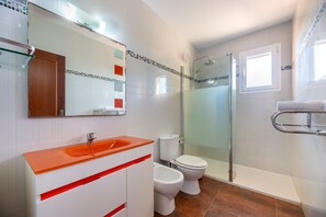 Ein Badezimmer mit Duschkabine aus Glas, einem weißen Waschbecken mit orangefarbener Arbeitsplatte, zwei Toiletten und einem Spiegel mit Holztür.