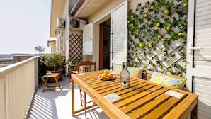 A wooden table with a bottle and a plate of fruit on a balcony with a view.