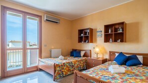 A hotel room with two beds, a balcony, wooden shelves with decorative items, and a view of the city.