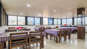 A dining area with tables set for four, each with a plaid tablecloth and a vase of flowers. The room has large windows offering a view of the cityscape. - MeroStay 186 Hotel RR (Kathmandu)