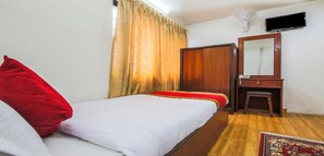 Una habitación de hotel con cama, un armario de madera, un televisor montado en la pared y un taburete pequeño.