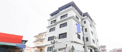 A multi-story building with a modern architectural design, featuring balconies and air conditioning units.