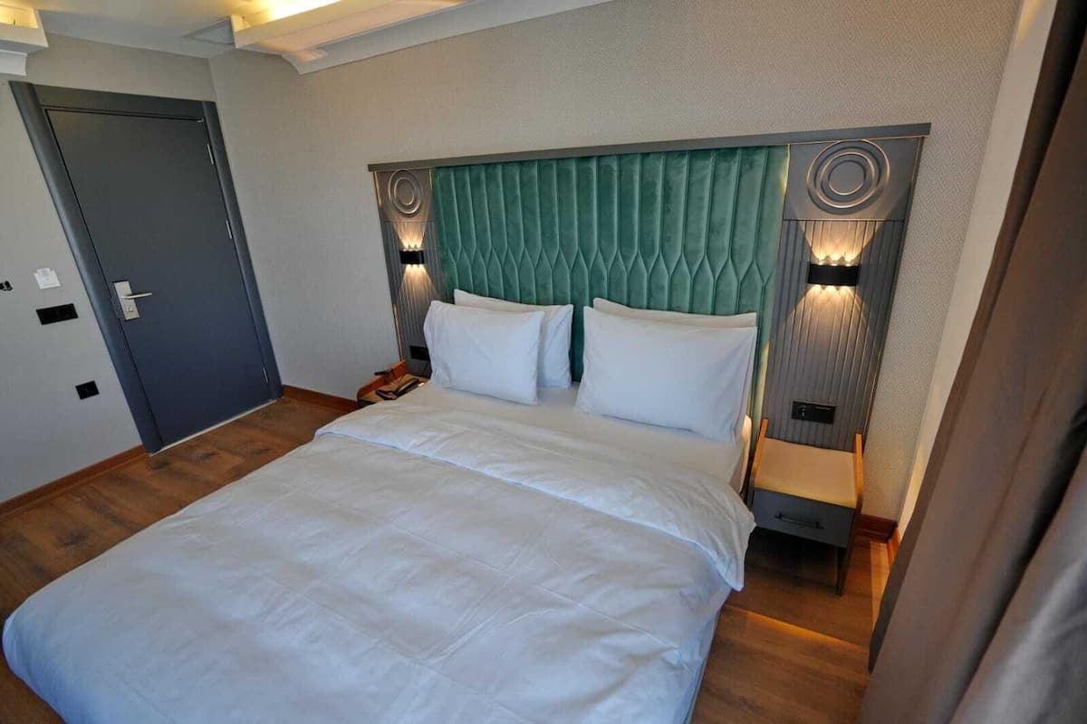 Ein Hotelzimmer mit einem großen Bett, einem grünen gepolsterten Kopfteil, Nachttischlampen und einer Tür.