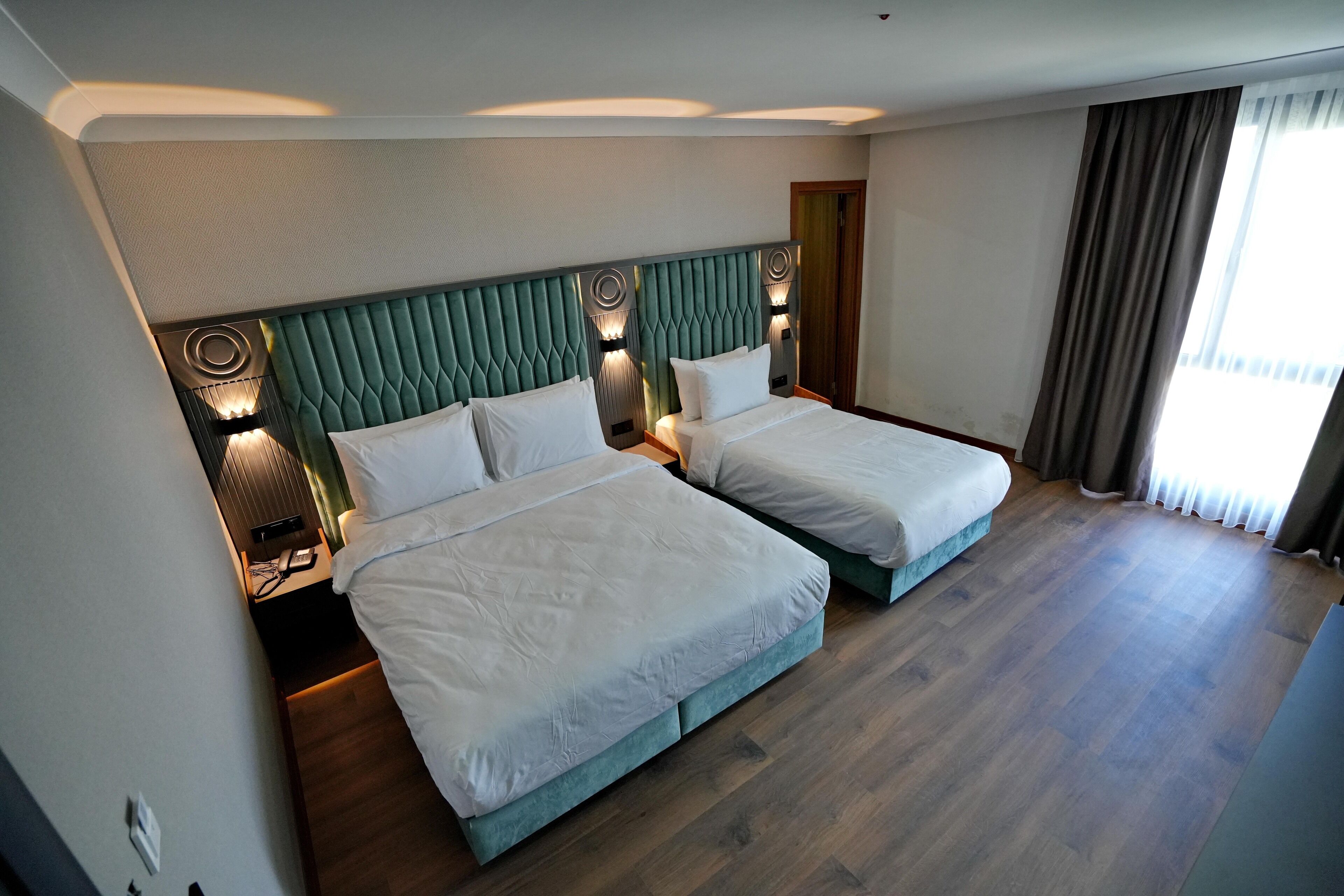 Quarto de hotel com duas camas, piso de madeira e uma janela grande com cortinas.