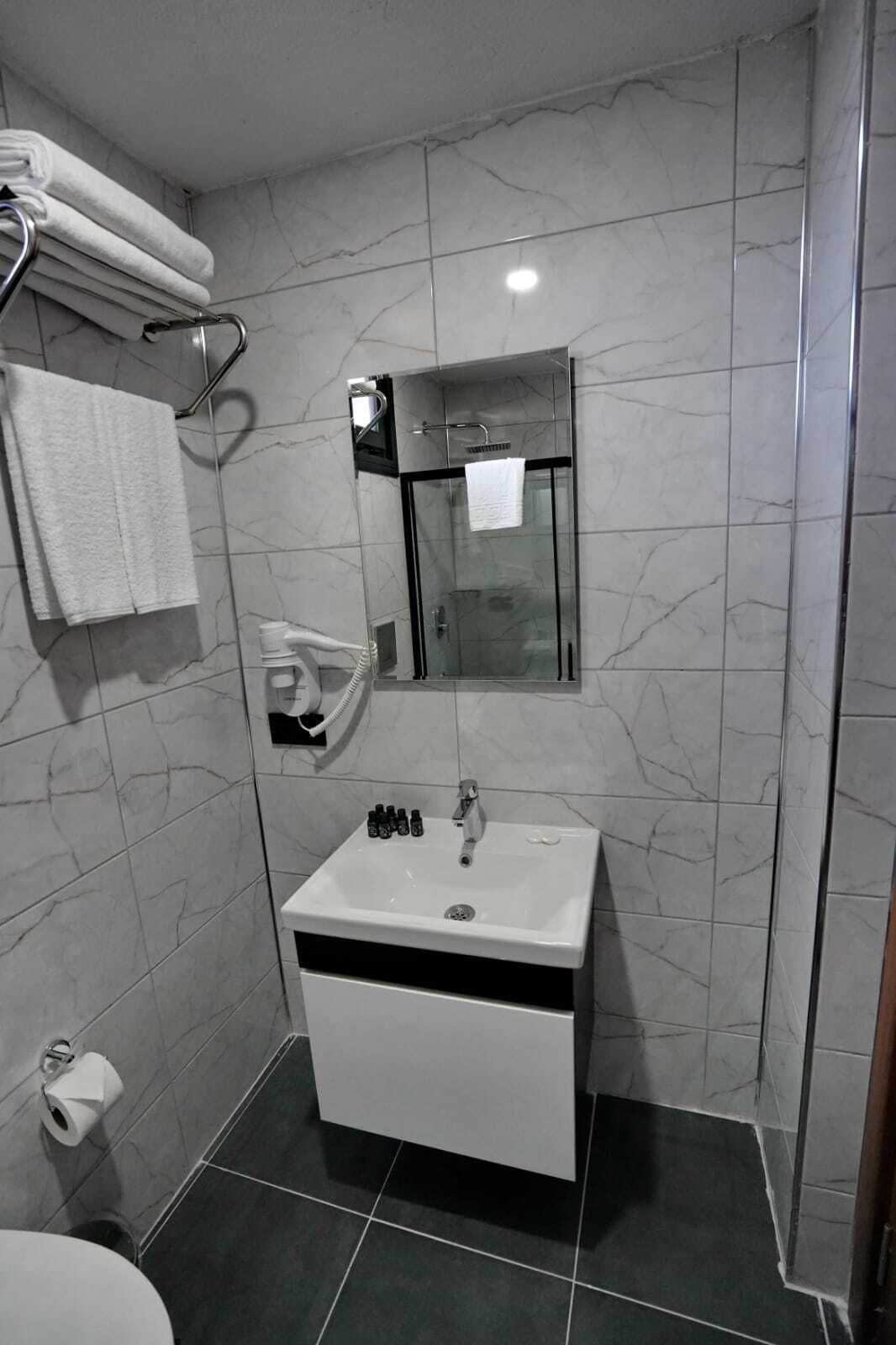 A modern bathroom with a glass-enclosed shower, a white sink with toiletries, and a towel rack.