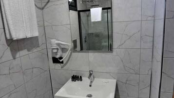 A modern bathroom with a glass-enclosed shower, a white sink with toiletries, and a towel rack.