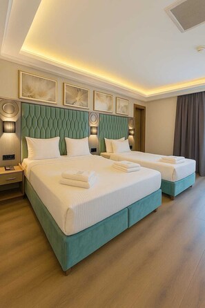 A hotel room with two beds, a green upholstered headboard, white linens, and a modern light fixture.