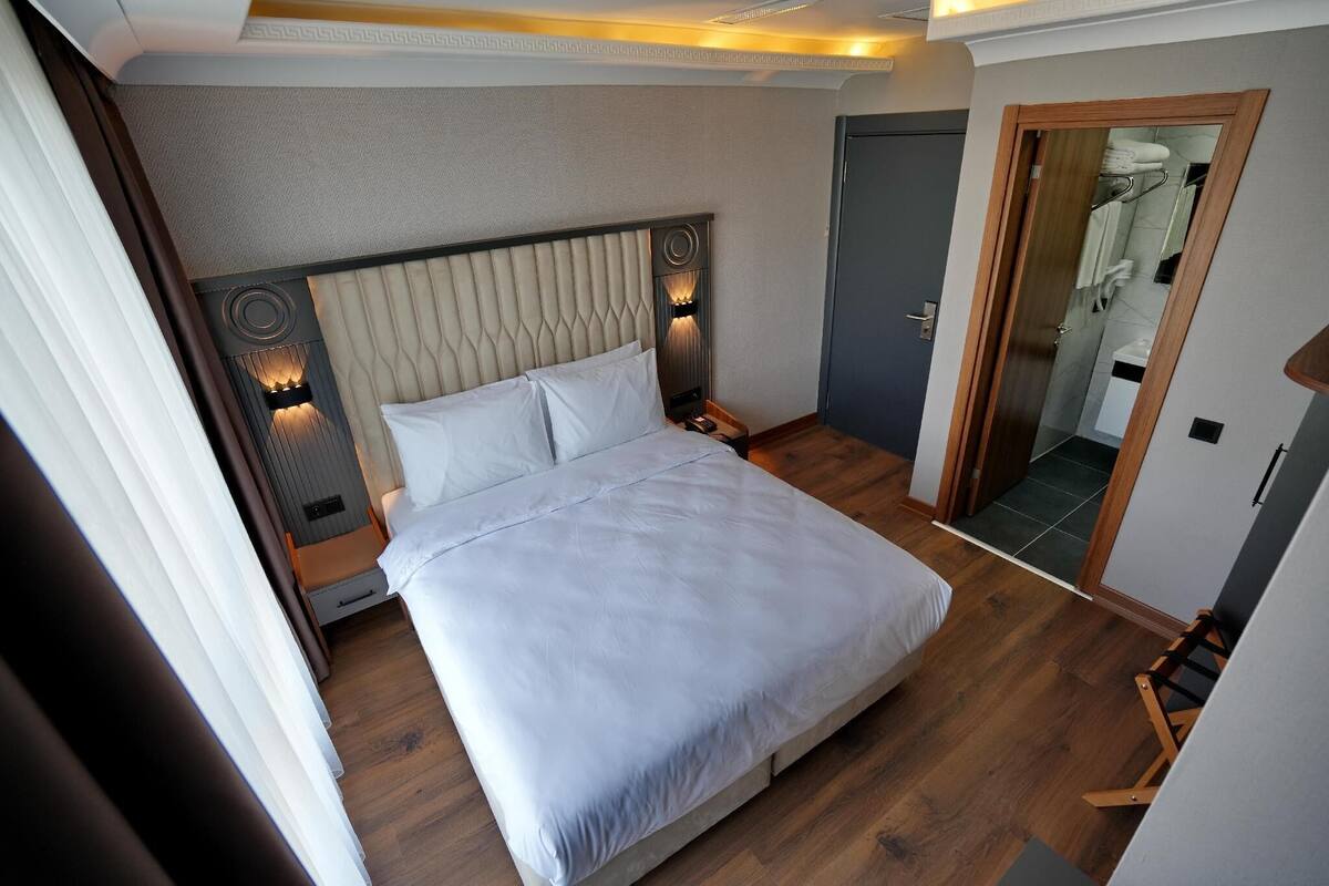 Une chambre d’hôtel moderne avec un grand lit, une table de chevet, une petite table et un luminaire fixé au mur.