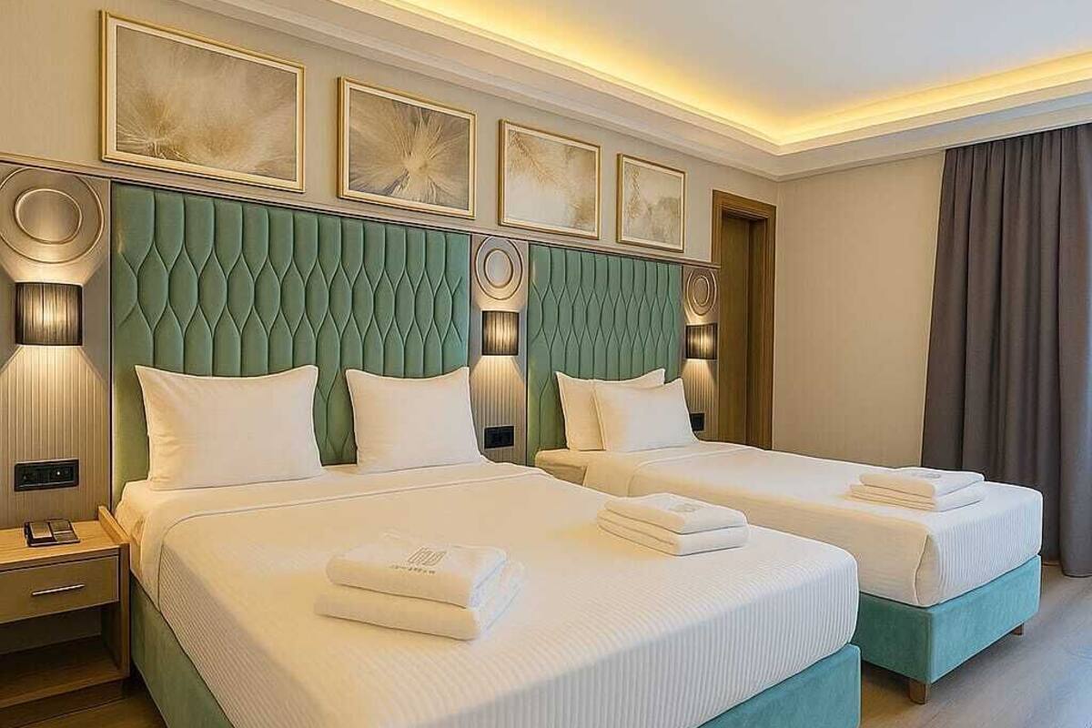 Une chambre d’hôtel avec deux lits, une tête de lit recouverte d’un tissu vert, du linge de lit blanc et un luminaire moderne.