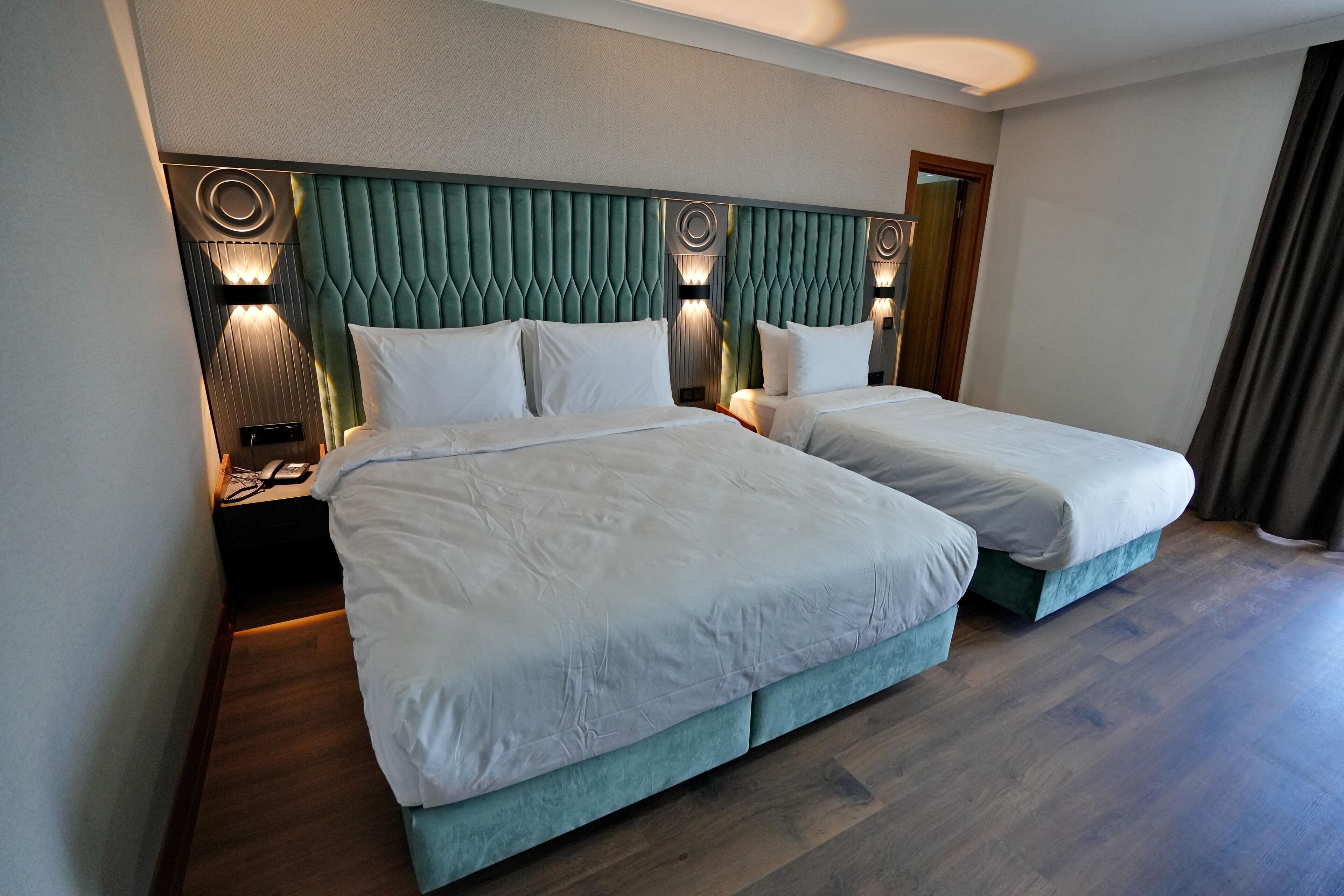 Ett hotellrum med två sängar, ett trägolv och en grön, klädd sänggavel.