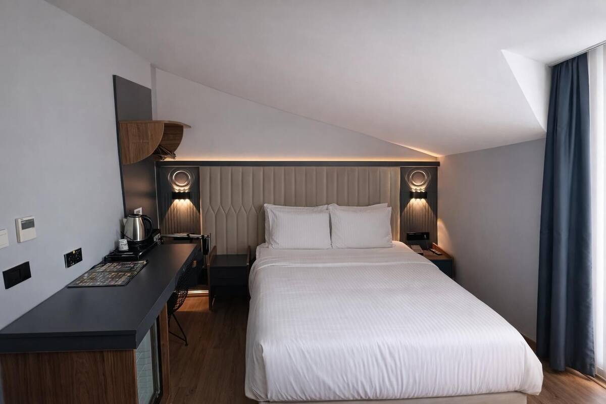 Une chambre d’hôtel moderne avec un grand lit, un bureau équipé d’une machine à café et deux lampes de chevet.