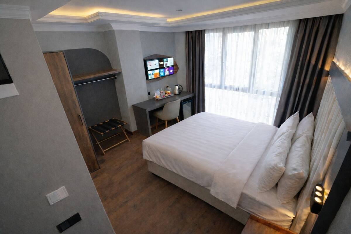 Une chambre d’hôtel avec un grand lit, un bureau avec un ordinateur, un petit coin salon et une vue sur l’extérieur.