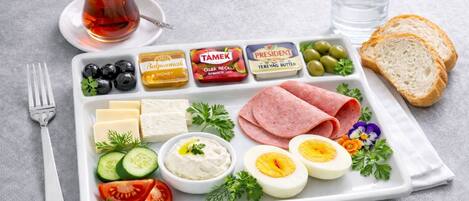 A meal tray with various food items including cheese, olives, tomatoes, cucumbers, and a cup of tea.