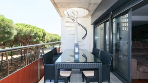 Een balkon met een glazen tafel en stoelen, een wenteltrap en uitzicht op bomen.