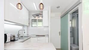 Una cocina moderna con armarios blancos, encimera de mármol y dos lámparas colgantes.