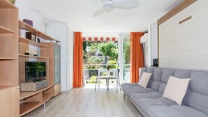 Una sala moderna con un sofá gris, mueble de entretenimiento de madera y un balcón con cortinas naranjas.
