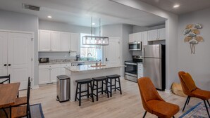 A modern kitchen with white cabinets, stainless steel appliances, and a central island with bar stools. - 3 Bedroom Townhome Suite (Ogden)