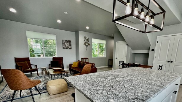 A spacious living area with a granite island, modern furniture, and large windows providing natural light. - 3 Bedroom Townhome Suite (Ogden)