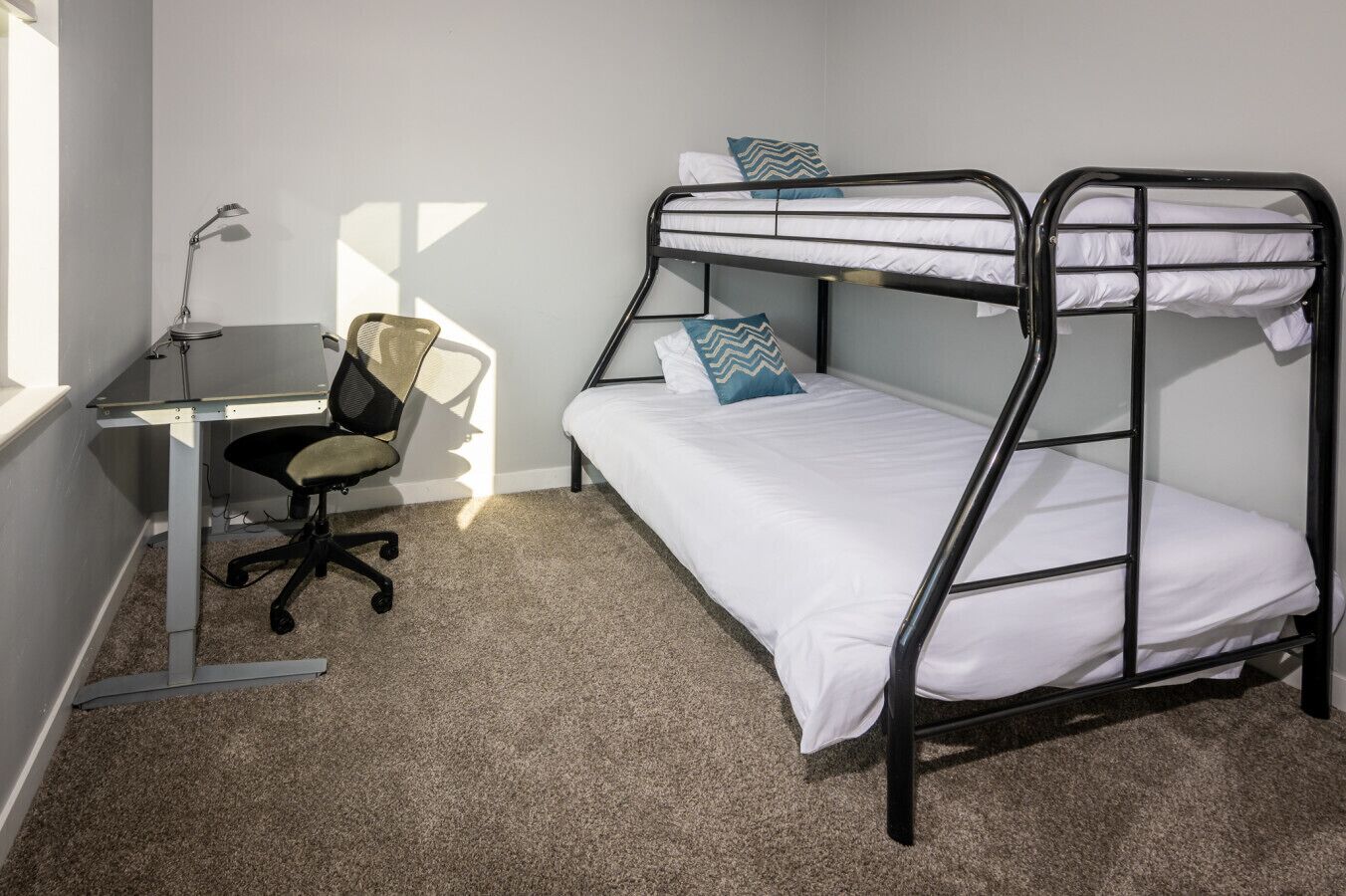 A bunk bed room with a desk and chair, a lamp, and a window.