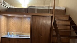 Une pièce de taille modeste avec un escalier en bois, une petite kitchenette et un lit superposé.