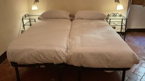 Un lit simple avec une literie blanche, deux tables de chevet avec des lampes et un sol carrelé.