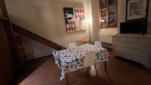 Un coin repas avec une table dressée pour deux personnes, une chaise, une petite table ronde, un téléviseur posé sur une commode et un escalier.