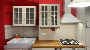 Une cuisine avec deux armoires blanches, un évier, une cuisinière à gaz et un mur rouge.
