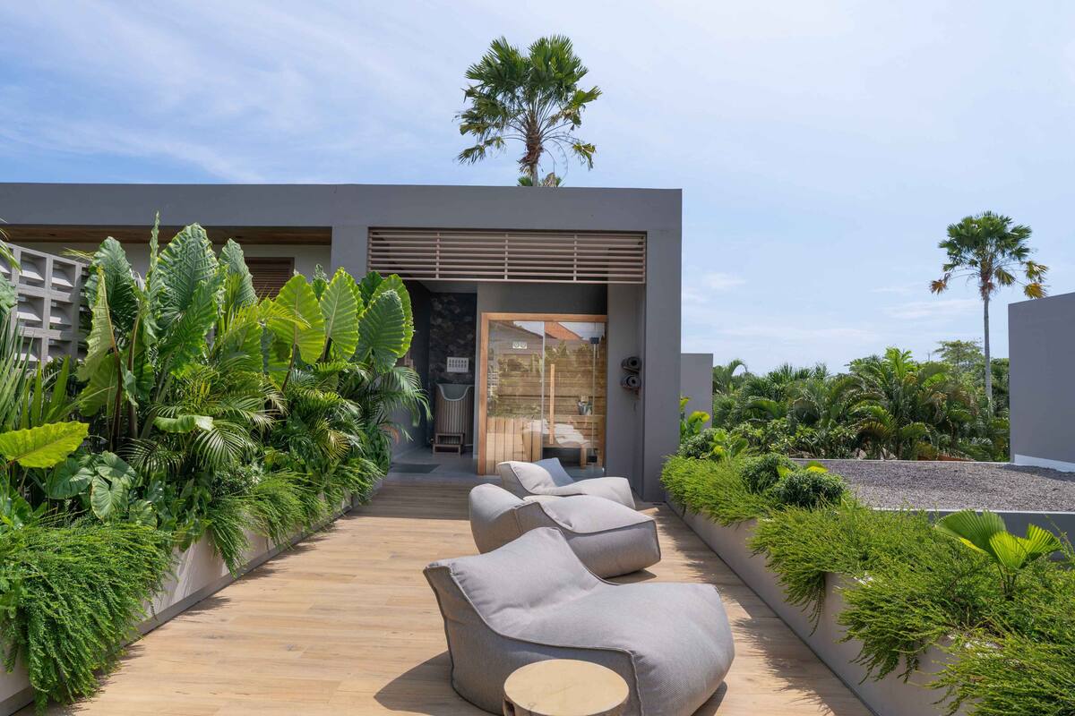 A modern outdoor seating area with cushioned chairs and a wooden deck, surrounded by lush tropical plants.
