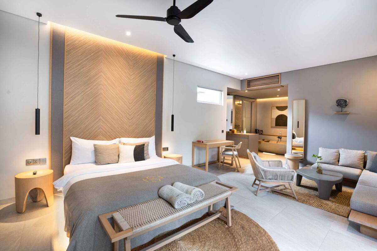 A modern hotel room with a large bed, a desk, a sofa, and a ceiling fan.