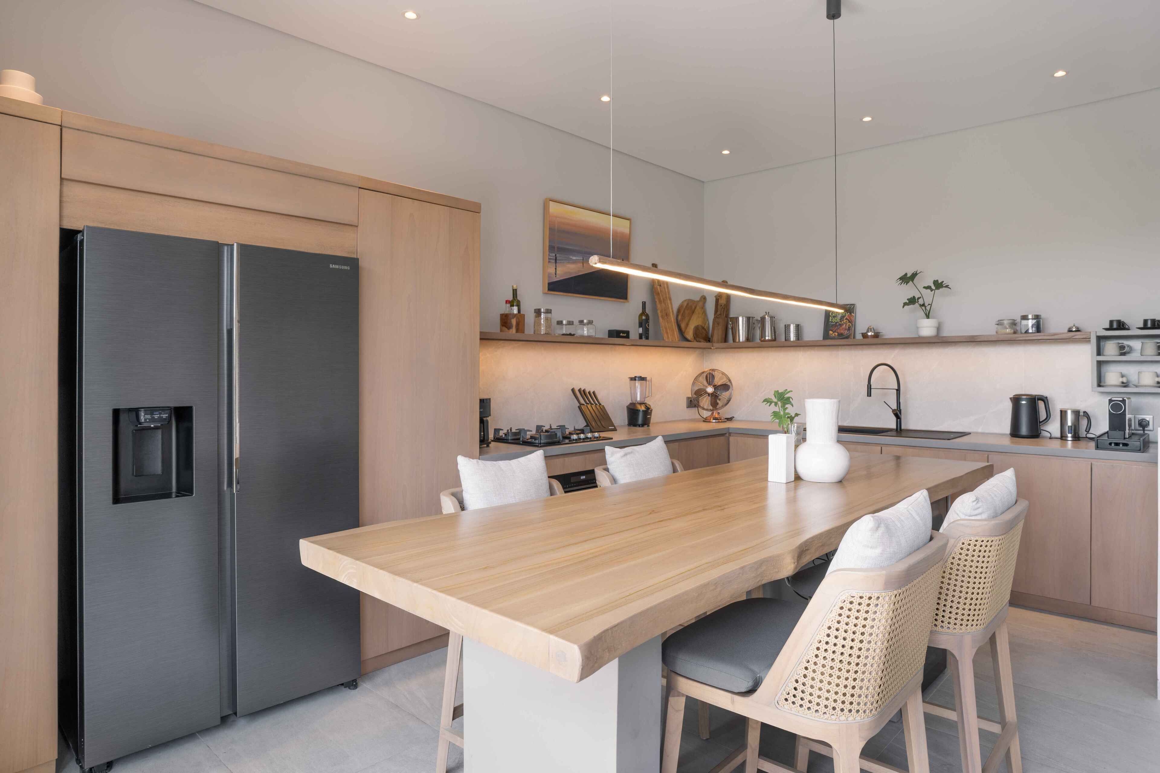 Una cocina moderna con refrigerador de acero inoxidable, mesa de comedor de madera y taburetes de bar.