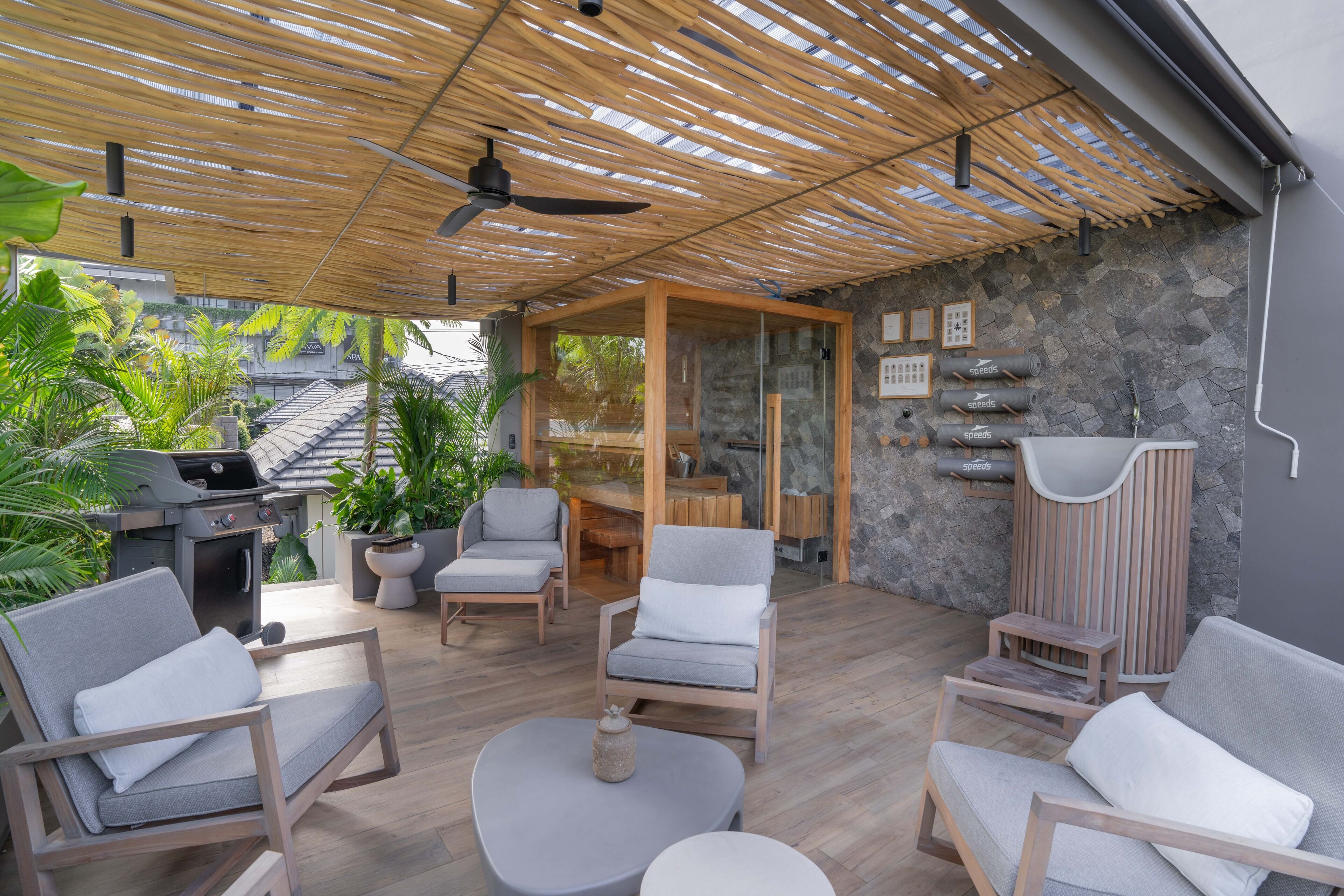 An outdoor patio with wooden furniture, a grill, and stone walls.