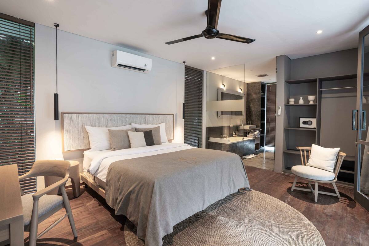 A modern bedroom with a large bed, a desk, a chair, a wardrobe, and a ceiling fan.