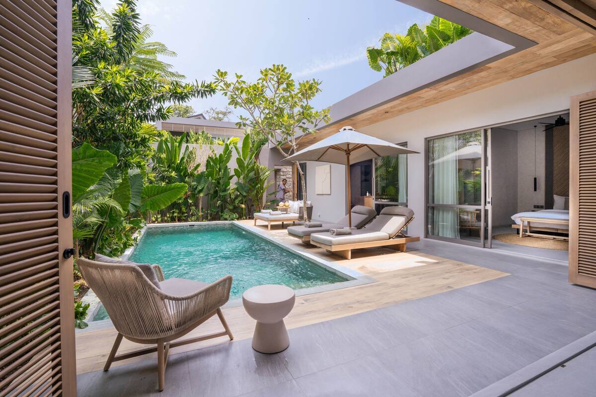 A modern outdoor pool area with lounge chairs and a table, surrounded by lush greenery.