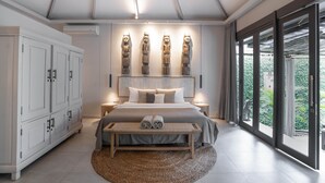 Un dormitorio moderno con una cama grande, un banco de madera, un ventilador de techo y vistas a zonas verdes.