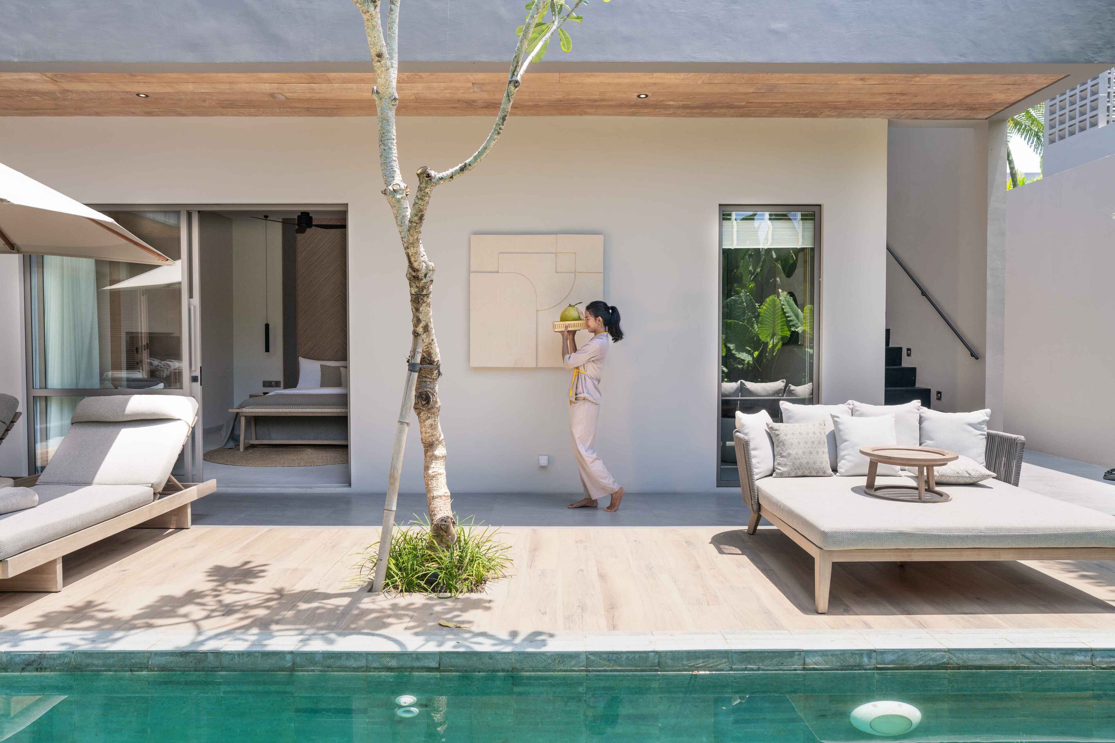 A modern outdoor living area with a pool, a wooden deck, and a minimalist interior with a sofa and a table.