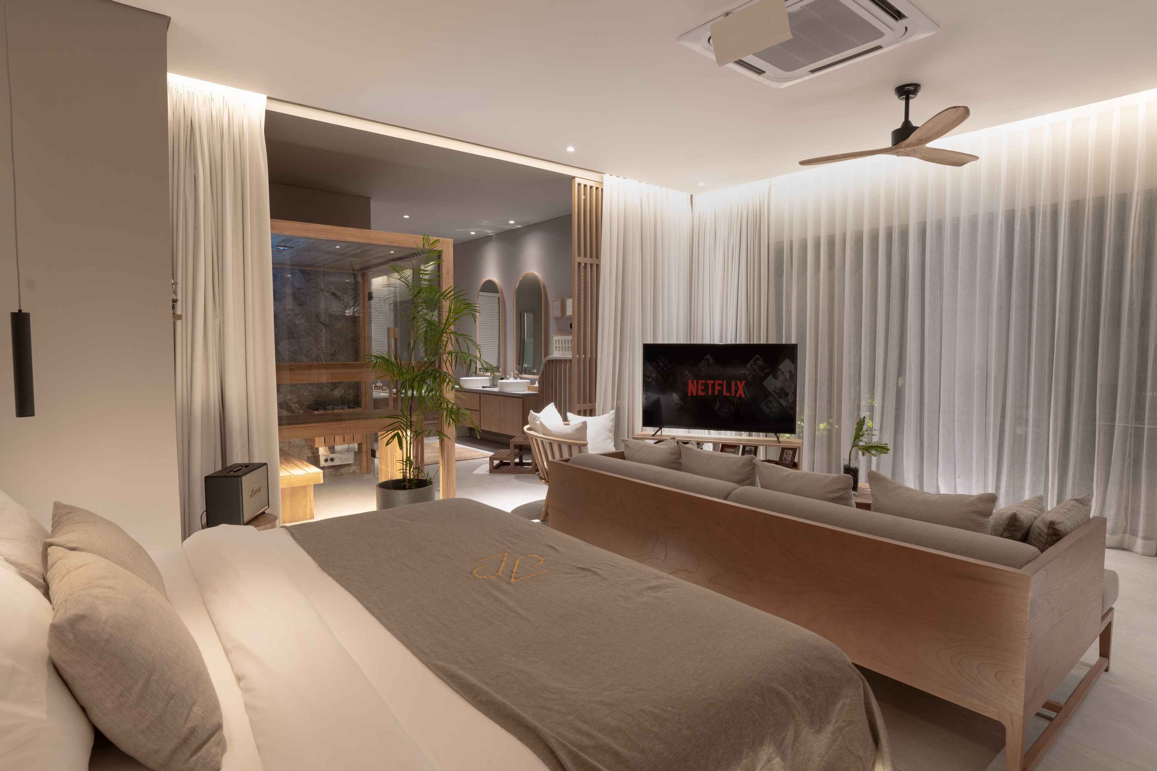 A modern hotel room with a large bed, a sofa, a TV, and a ceiling fan.