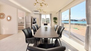 Un comedor moderno con una mesa grande, sillas negras, una lámpara única y vistas al mar a través de amplios ventanales.