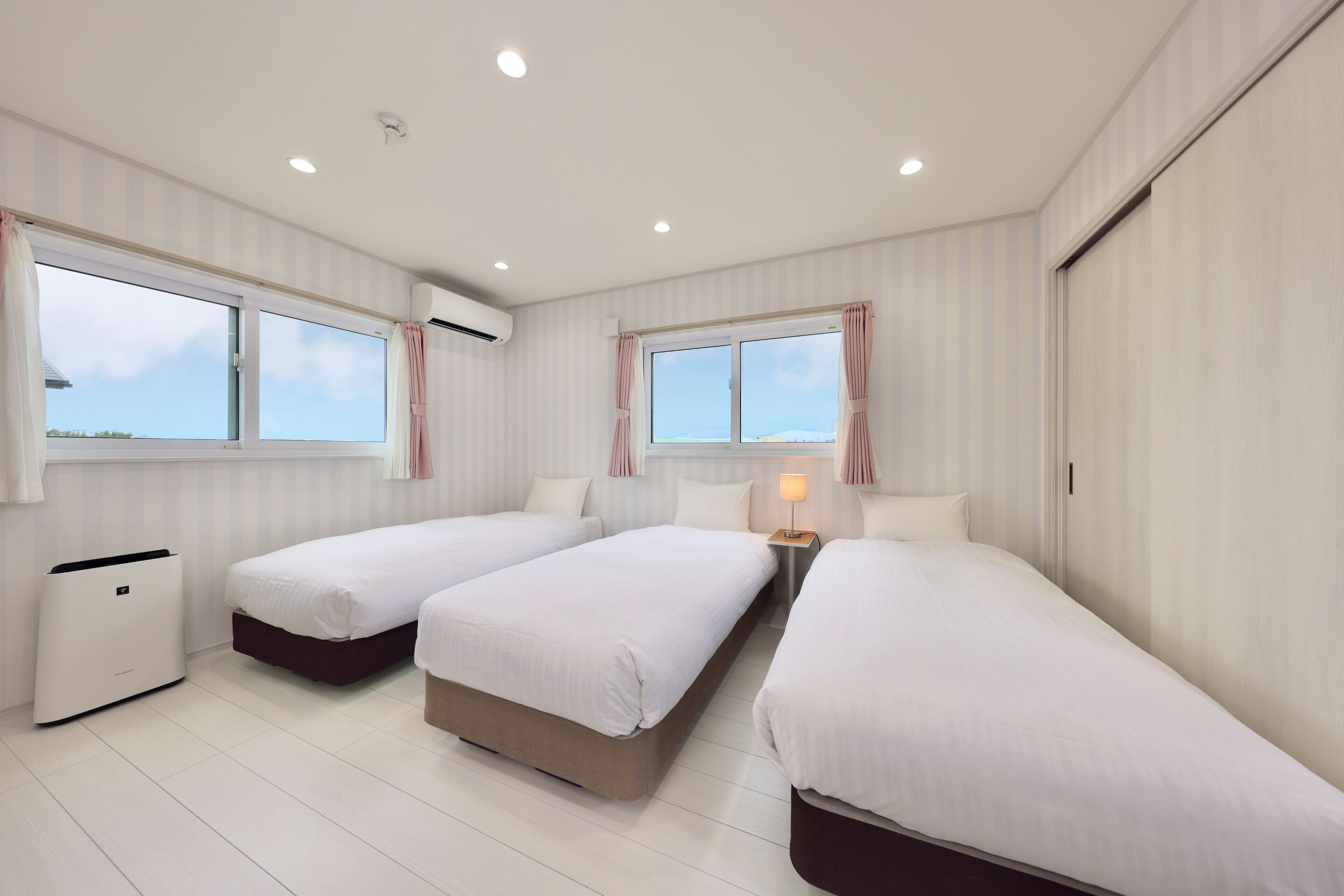 Una habitación de hotel con dos camas individuales, una mesita de noche con lámpara y una ventana con cortinas.