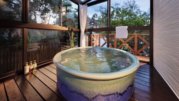 Un jacuzzi en una terraza de madera con vistas a árboles a través de amplios ventanales.