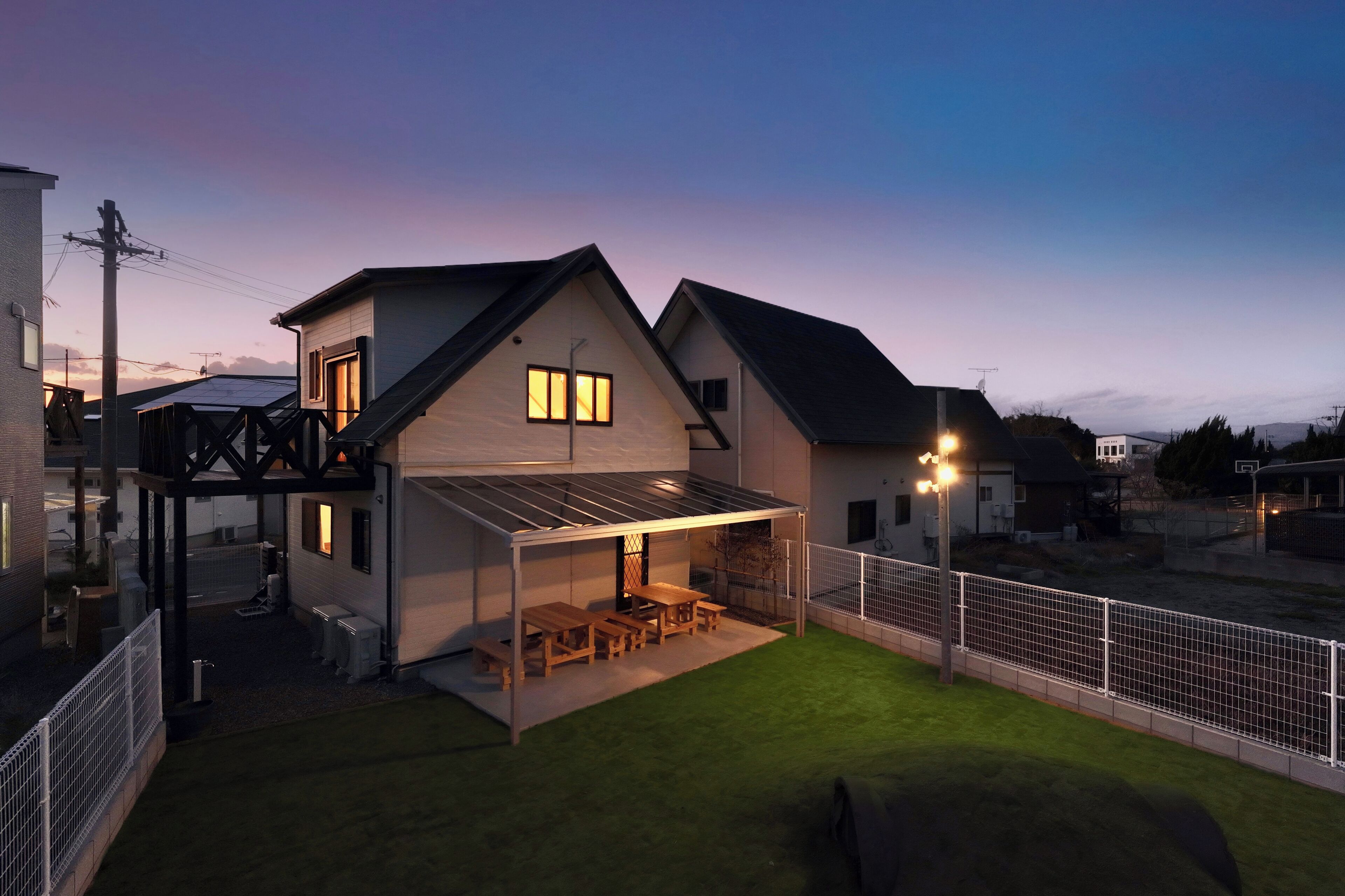 Ein modernes Haus mit überdachter Terrasse, einem umzäunten Garten und einem gepflegten Rasen.