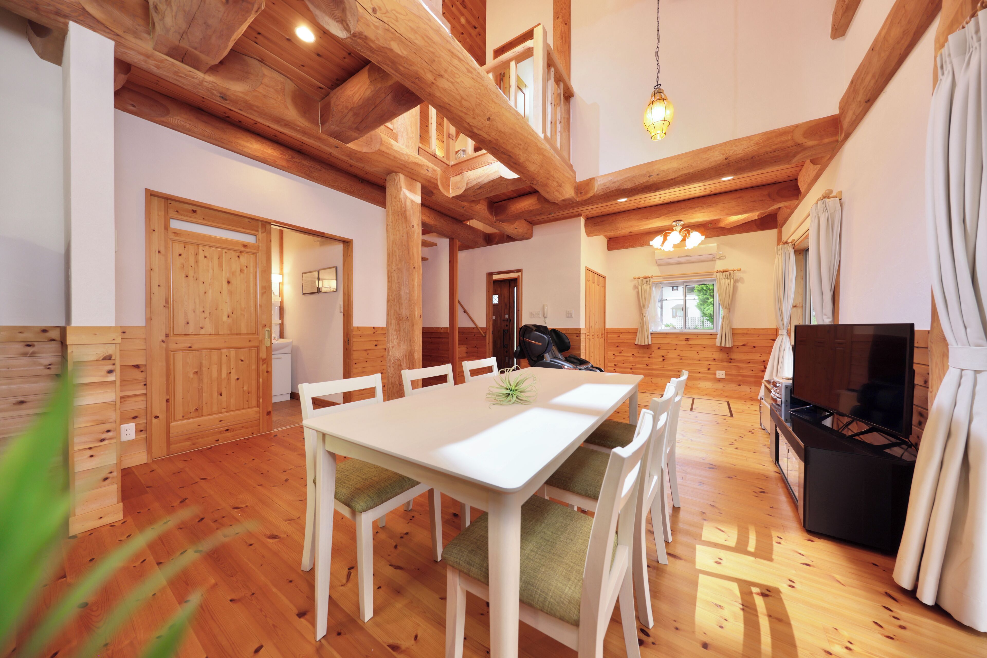 A spacious dining area with a white table and chairs, wooden beams on the ceiling, and a television in the corner.