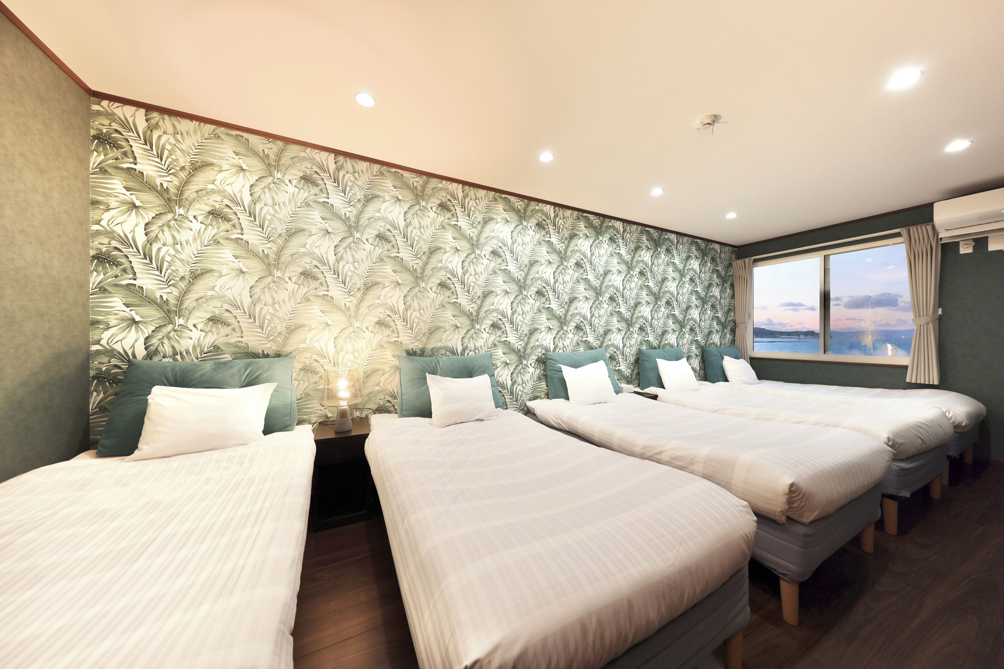 A hotel room with two single beds, a large window with a view, and a textured wall.