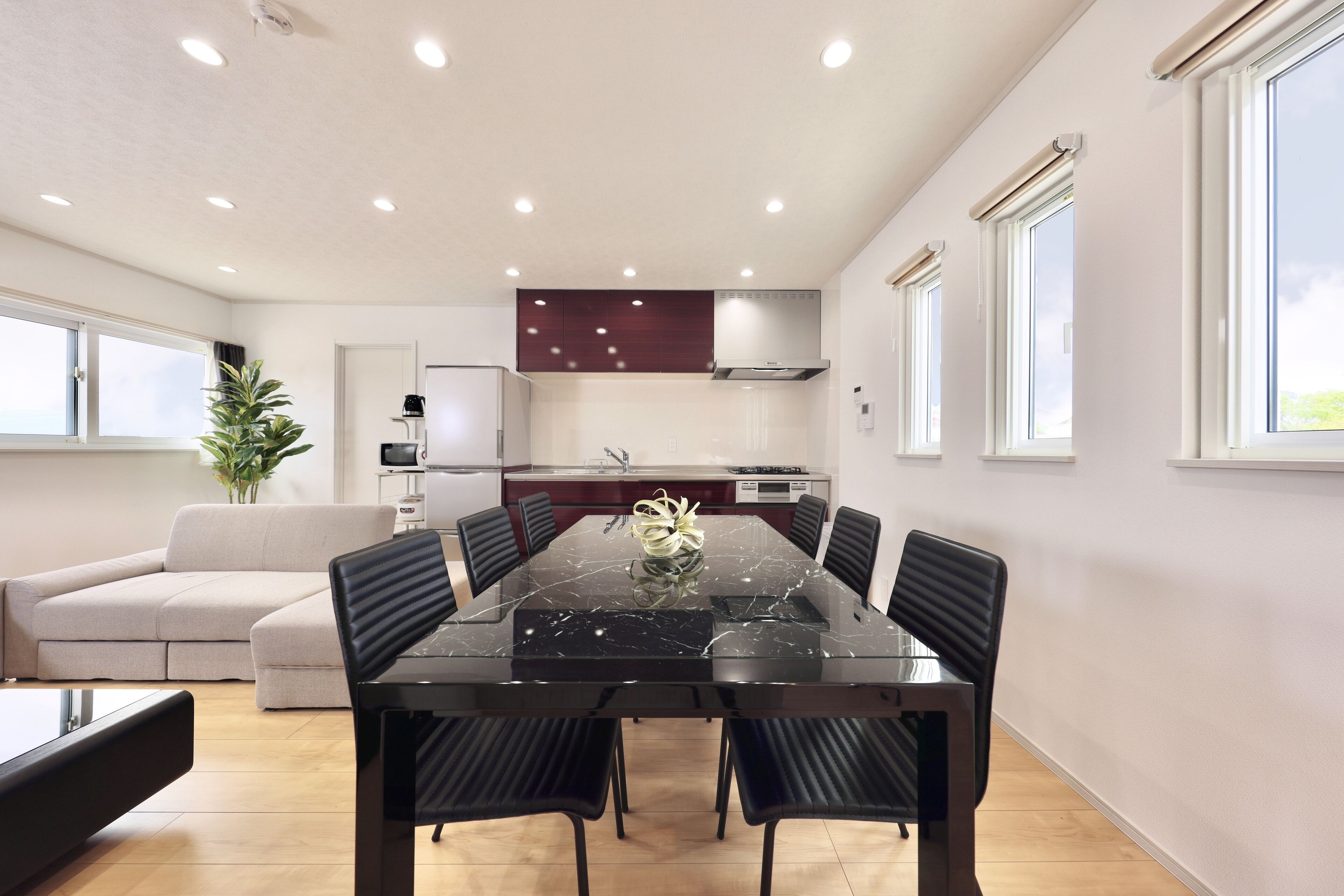 A modern dining area with a marble table, black chairs, a sofa, and a kitchen in the background.