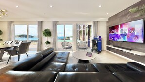 Una sala de estar moderna con un sofá de cuero negro grande, una mesa de comedor con sillas, una mesa de centro redonda y un televisor de pantalla plana montado en la pared.