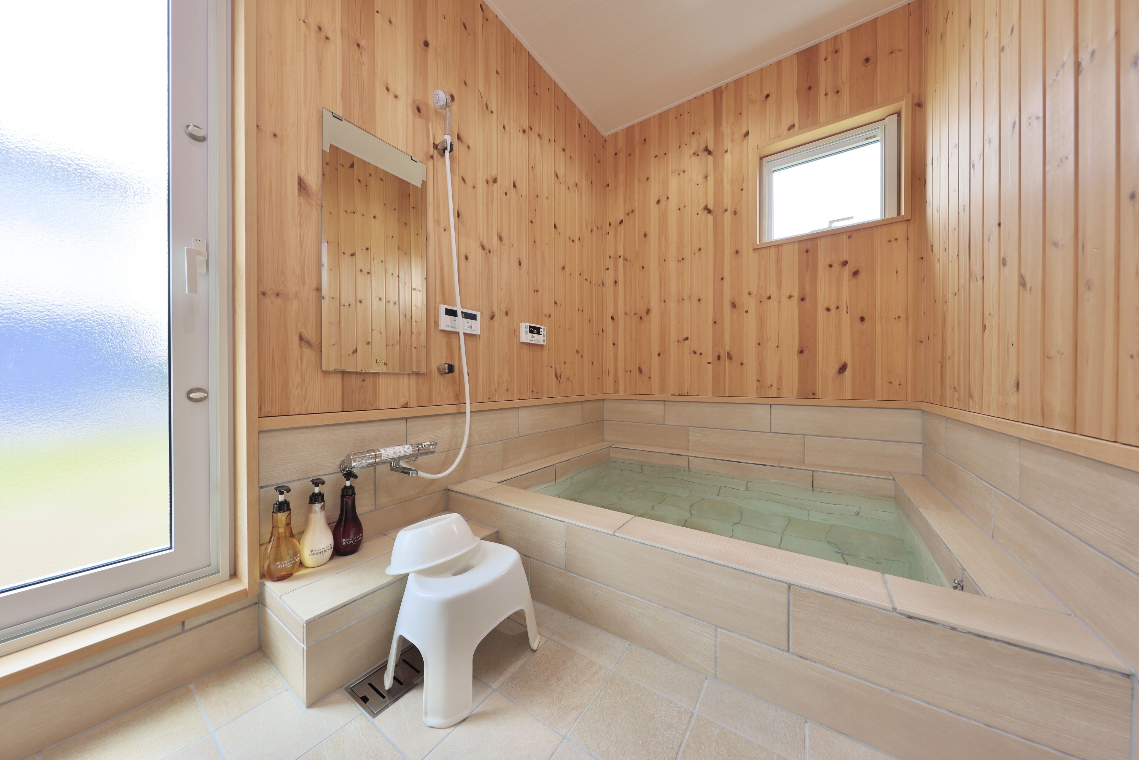 A modern bathroom with wooden paneling, a large bathtub, a small stool, and a window.